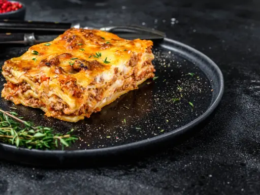 En bit gyllene lasagne på en svart tallrik, perfekt comfort food med köttfärs och ost.