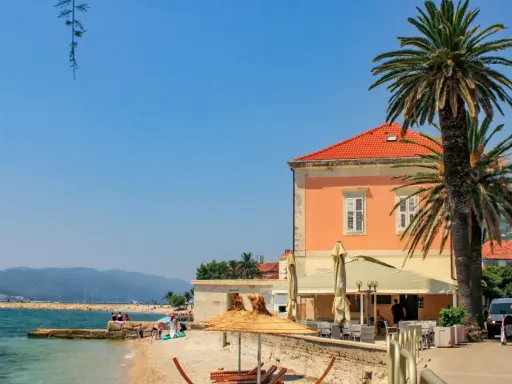 Słoneczny dzień na plaży na półwyspie Pelješac. Palmy, kamienny murek, tawerna i turkusowe morze.