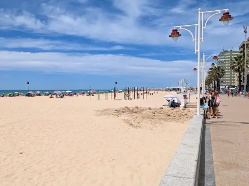 Sonniger Tag am Playa Victoria in Cádiz. Menschen entspannen sich unter bunten Sonnenschirmen, während Kinder am Strand spielen.