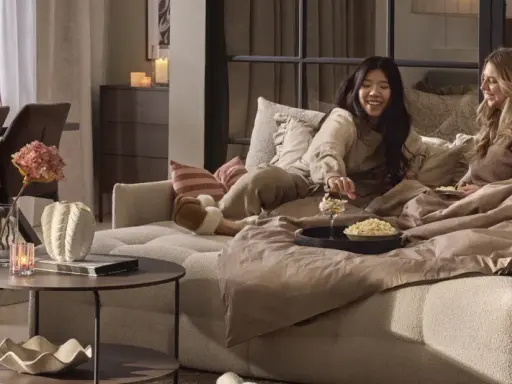 Två vänner myser i en stor sov fåtölj med popcorn och filtar.