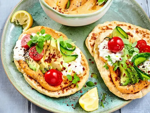 Leckere kalte gerichte ohne kochen: Fladenbrot mit Hummus, Avocado, Tomaten, Gurke und Frischkäse. Garniert mit Kräutern und Zitrone.