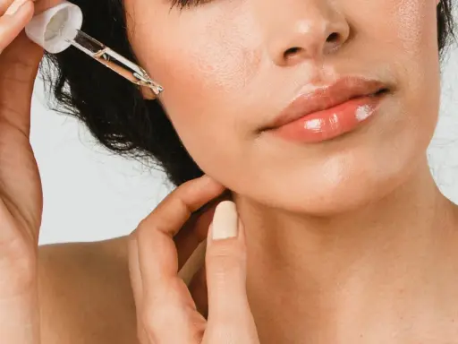 Une main applique une goutte d'huile de ricin visage sur la peau. Les lèvres sont brillantes, la peau est lumineuse.