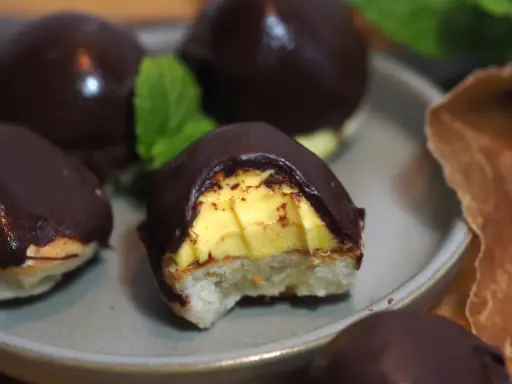 Chokladöverdragna biskvier med gul kräm och en bit av en mintkvist. Perfekt för att frysa in och njuta av senare.