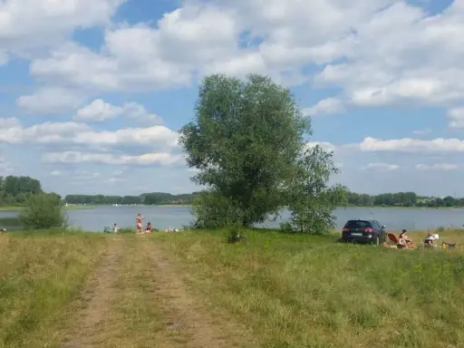 Słoneczny dzień nad jeziorem przeczyckim. Ludzie odpoczywają na trawie, w tle widać wodę i drzewa.