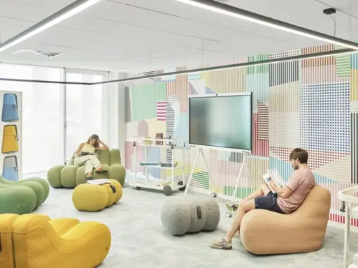Un espace de repos coloré avec des poufs confortables et un mur à motifs géométriques. Deux personnes lisent tranquillement.