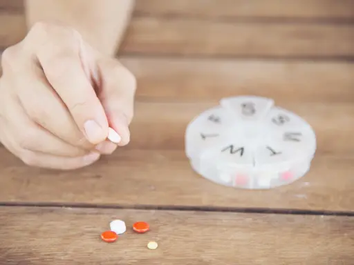 Dłoń trzyma tabletkę. Obok leżą inne pigułki i pojemnik na leki. Captopril 12,5 mg jak długo działa?