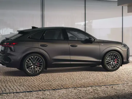 Elegancki Audi Q3 2025 w ciemnym kolorze, z dynamiczną linią nadwozia, prezentuje się na tle nowoczesnej architektury.