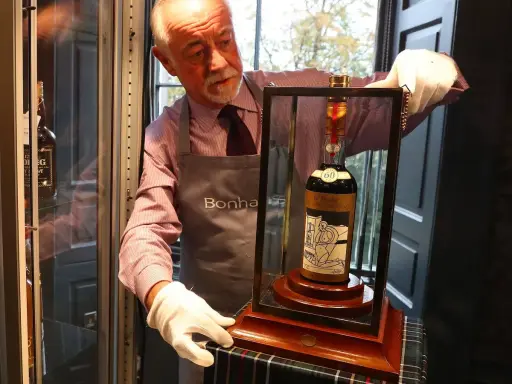 Mann mit weißen Handschuhen präsentiert eine Flasche des teuersten Weins der Welt, eine seltene Macallan 60 Year Old.