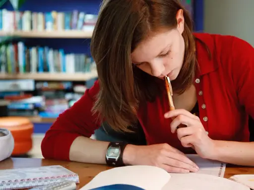 Dziewczyna w czerwonym swetrze myśli nad tekstem rozprawki maturalnej, trzymając długopis przy ustach.