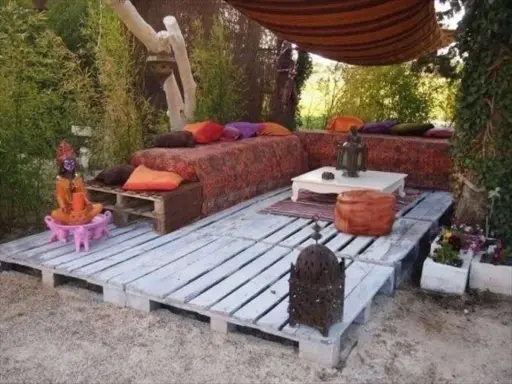Un rincón zen con sofás y mesas bajas creados con jardineras con palets, cojines coloridos y faroles.
