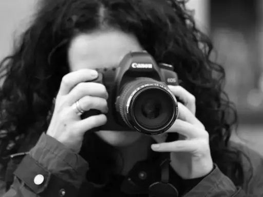 Czarno-białe zdjęcie kobiety z kręconymi włosami, która trzyma aparat Canon. To jej pierwsze szkolenie z fotografii.