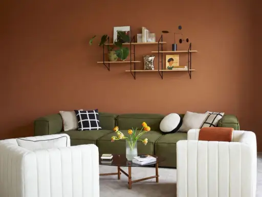 Salon cosy aux murs couleur cognac, canapé vert, fauteuils blancs et table basse.