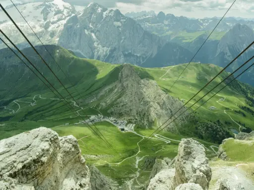 Vista mozzafiato dal passo Pordoi, con montagne innevate, verdi pendii e una strada tortuosa.