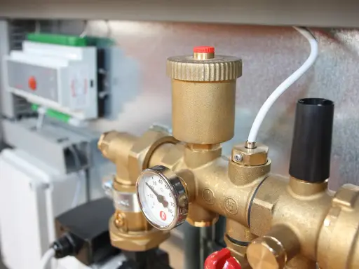 Detalle de tuberías de latón con manómetro y una válvula de seguridad. En el fondo, un panel de control.