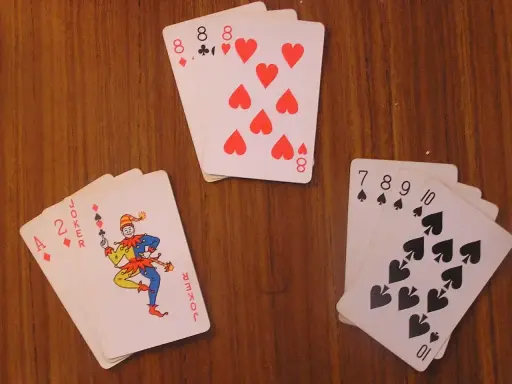 Karty na drewnianym stole: as, dwójka, joker i inne. Joker w kartach wygląda jak wesoły błazen.
