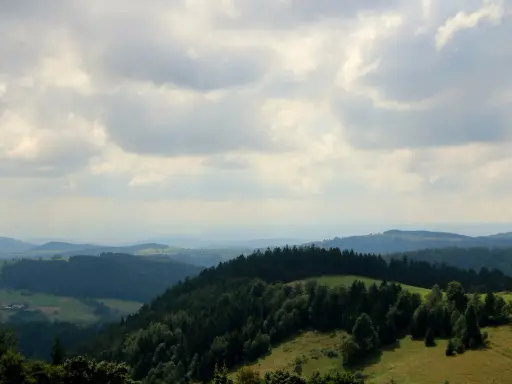Malownicze **góry Sowie** oferują liczne **atrakcje** turystyczne. Widok na zielone wzgórza i lasy pod zachmurzonym niebem.