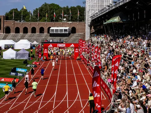 Löpare korsar mållinjen på stockholm marathon bana. Publiken jublar från läktaren.