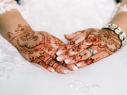 Manos de novia con intrincados diseños de henna, anillos y pulsera brillante, listas para la boda.