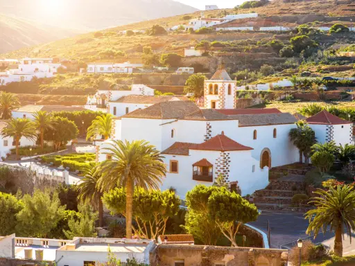 Villaggi turistici a Fuerteventura, con case bianche, palme e una chiesa con campanile, immersi nel sole dorato del tramonto.