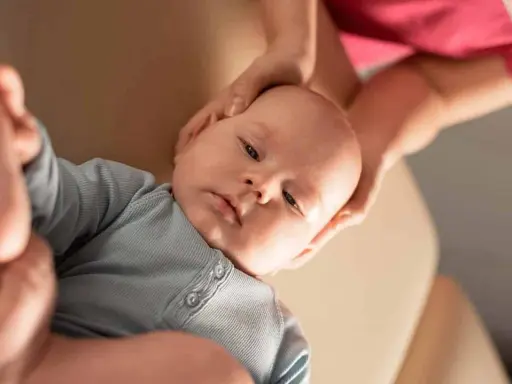 Delikatne dłonie osteopaty pediatrycznego obejmują główkę niemowlęcia, zapewniając mu komfort i wsparcie podczas terapii.