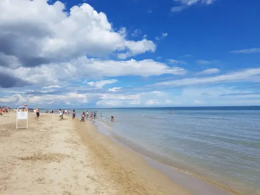 Una giornata di sole sulla spiaggia del cuore Riccione, con bambini che giocano e adulti che si godono il mare calmo sotto un cielo azzurro e nuvoloso.