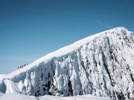 En grupp skidåkare på en helags topptur, med en dramatisk snöklädd bergssida och klarblå himmel.