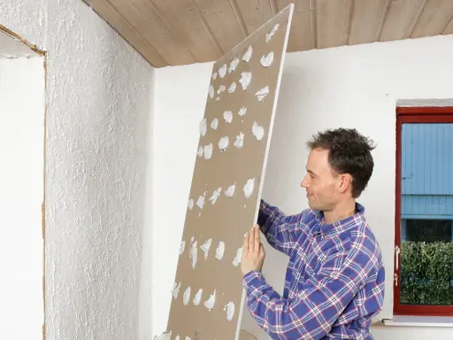 Man håller upp en gipsskiva med spackelklumpar, redo att måla direkt på gips.
