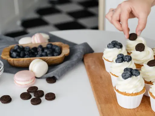 Des cupcakes décorés avec une crème chiboust aérienne, des myrtilles et des biscuits. Des macarons et des myrtilles sont disposés à côté.