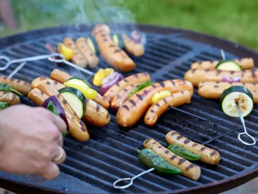 Grillad korv med grönsaker på en het grill. Röken stiger och doften sprider sig.