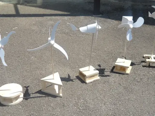 Cinq maquettes éoliennes, fabrication simple en bois, alignées sur un sol gris.