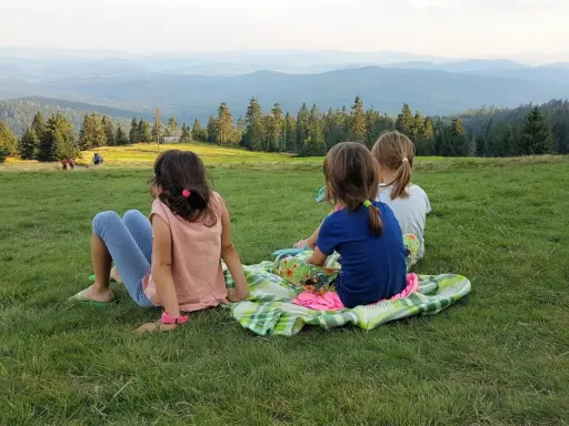 Trzy dziewczynki siedzą na trawie, podziwiając krajobraz. Beskid Żywiecki oferuje wspaniałe atrakcje dla dzieci, jak ten widok.