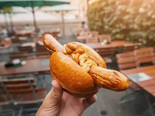 Eine Hand hält eine Bratwurst im Brötchen mit Senf. Ein leckerer Snack, aber die Bratwurst Kalorien sollte man im Auge behalten.