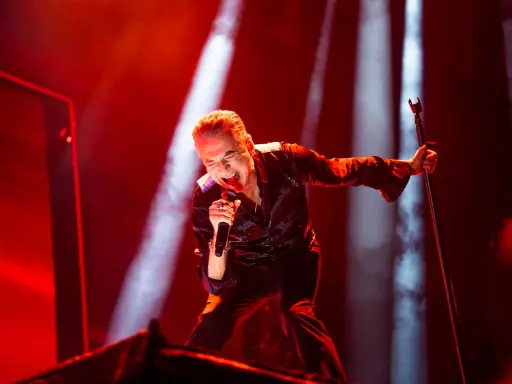 Dave Gahan sjunger passionerat under en Depeche Mode konsert, badad i rött ljus.