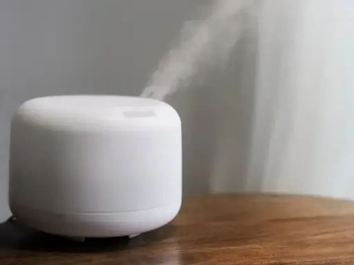 Humidificador casero blanco emitiendo vapor sobre una mesa de madera.