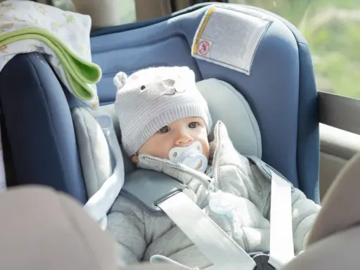 Bebé con gorro de oso y chupete en un alzador o silla coche, listo para un viaje seguro.