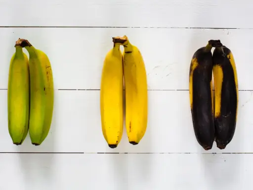 Drei Paare Bananen zeigen verschiedene Stadien der Reife: grün, gelb und überreif. So kann man sehen, wie Bananen lagern.