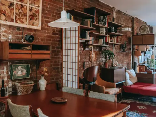 Wnętrze kawalerki z ceglaną ścianą, drewnianym stołem i meblami w stylu vintage.