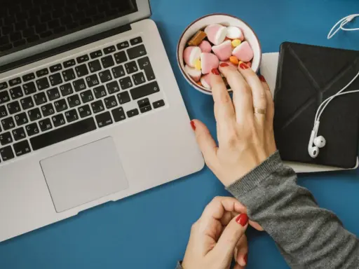 Eine Hand greift nach Süßigkeiten neben einem Laptop. Das Bild symbolisiert assoziatives Lernen: Belohnung und Fokus.
