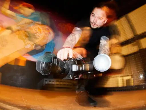 Fotograf z tatuażami łapie ruch deskorolkarza z Red Bulla. Krótki czas naświetlania uchwycił dynamiczną akcję.