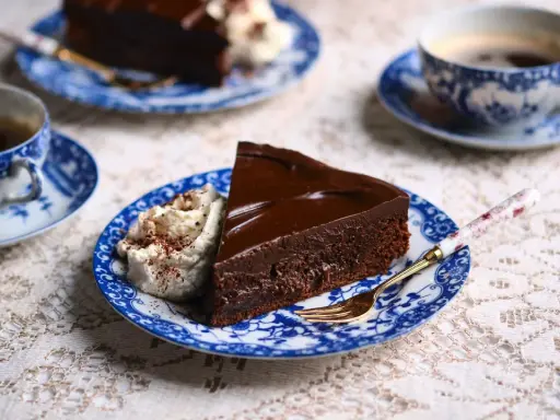 En bit chokladkaka med glansig ganache och vispgrädde, serverad med kaffe. Perfekt för ett enkelt ganache recept.