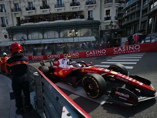 Lewis Hamilton im Ferrari-Boliden rast durch Monaco. Zuschauer säumen die Strecke, die Casino-Werbung blinkt.