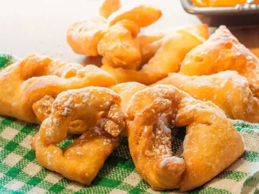 Beignets dorés saupoudrés de sucre glace sur un torchon à carreaux verts.