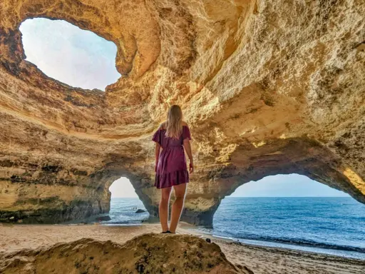 Frau steht in Höhle, blickt auf Meer. Ein Highlight der Algarve.