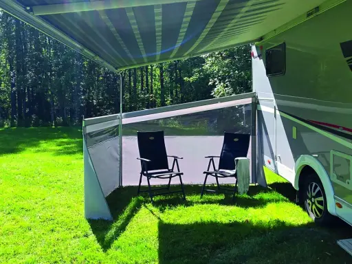 Ett vindskydd från Biltema ger skugga och skydd vid husbilen. Två stolar står redo för avkoppling i gräset.