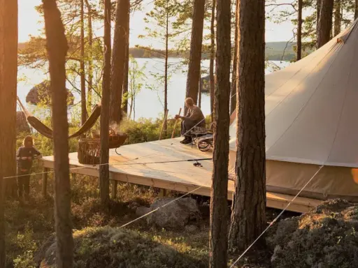 Kloten Nature Resort: en man sitter på en altan vid en sjö, bredvid ett stort tält. En hängmatta och en eldskål syns också.