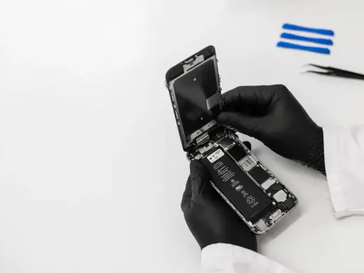 Ręce w czarnych rękawiczkach rozbierają iPhone'a, który wpadł do wody, ale działa. Widać baterię i wnętrze telefonu.