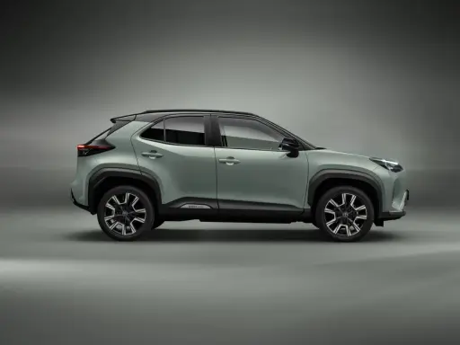 Nowy, zielony toyota crossover Yaris Cross z czarnym dachem i felgami stoi na szarym tle.