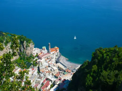 Vista dall'alto di Amalfi, con il mare blu e una barca a vela. La distanza tra Ravello e Amalfi è breve, ma il panorama è mozzafiato.