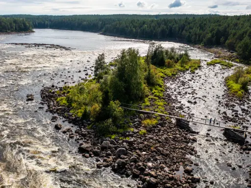 Vattenfall och en träbro över en stenig flod i Kalix, Sverige. Två personer går över bron.
