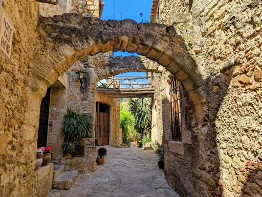 Antiker Durchgang in Pals, Spanien, mit steinernen Bögen und mediterraner Vegetation.